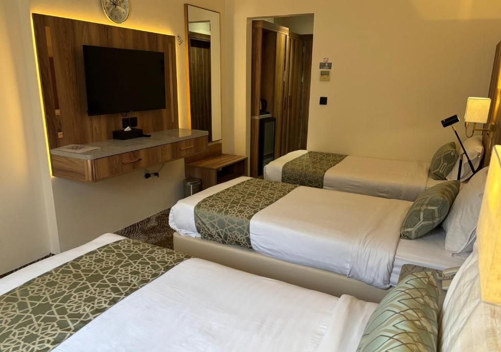 Habitación de hotel con dos camas, televisor, espejo y escritorio con lámpara.