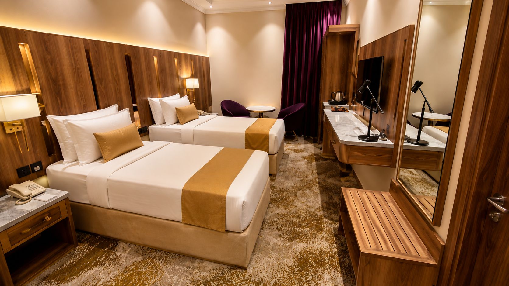 A hotel room with two beds, a desk, a chair, a mirror, and a telephone.