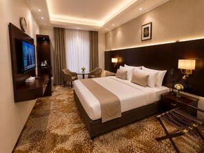 Habitación de hotel con una cama grande, televisión, escritorio, silla, lámpara y una pequeña mesa con flores.