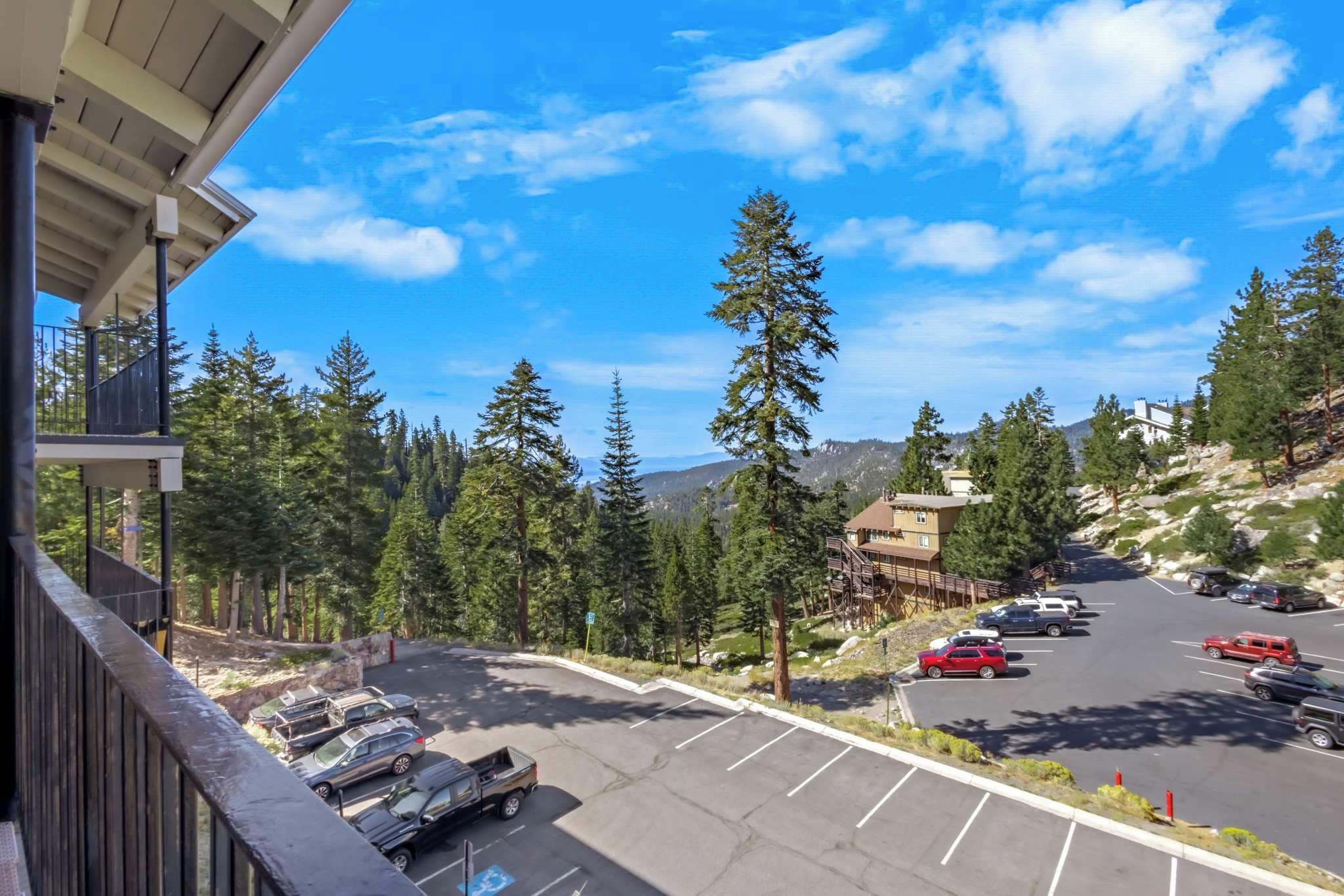 A parking lot with cars, a building with a sloped roof, and a mountainous landscape with trees.
