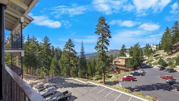 A parking lot with cars, a building with a sloped roof, and a mountainous landscape with trees.