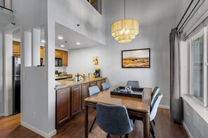 A modern kitchen with wooden cabinets, a dining area with a wooden table and chairs, and a large window with curtains. - Après Tahoe - 4BR Mountain Home (Stateline)