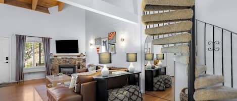 A spacious living room with a fireplace, a sofa, a coffee table, and a staircase with a unique design.