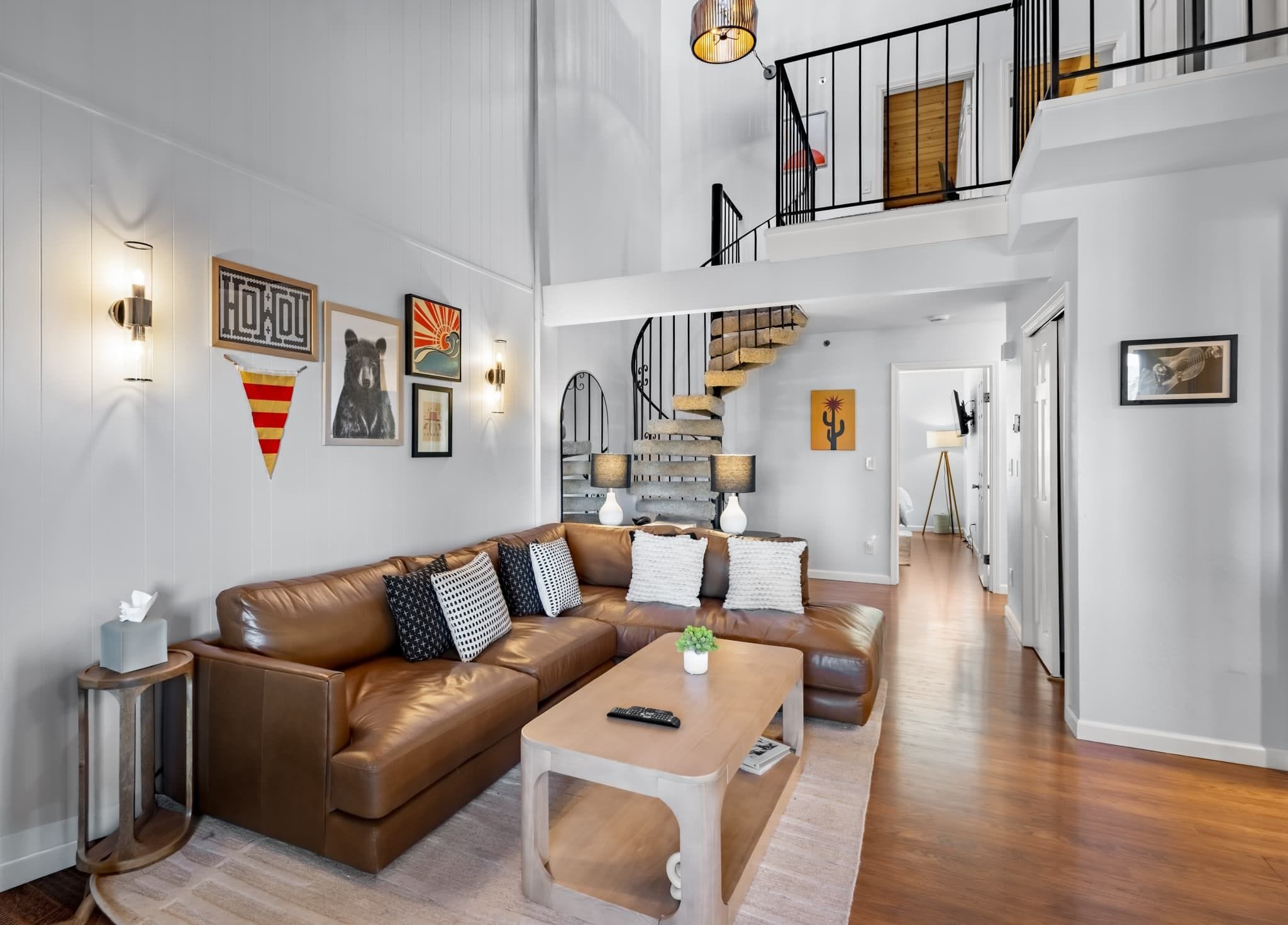 A spacious living room with a brown leather sofa, a coffee table, and a staircase leading to an upper level.