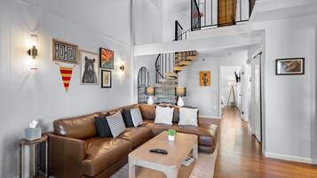 A spacious living room with a brown leather sofa, a coffee table, and a staircase leading to an upper level.