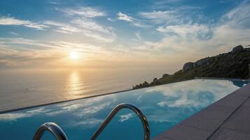 An infinity pool with a clear view of the ocean and a sunset.