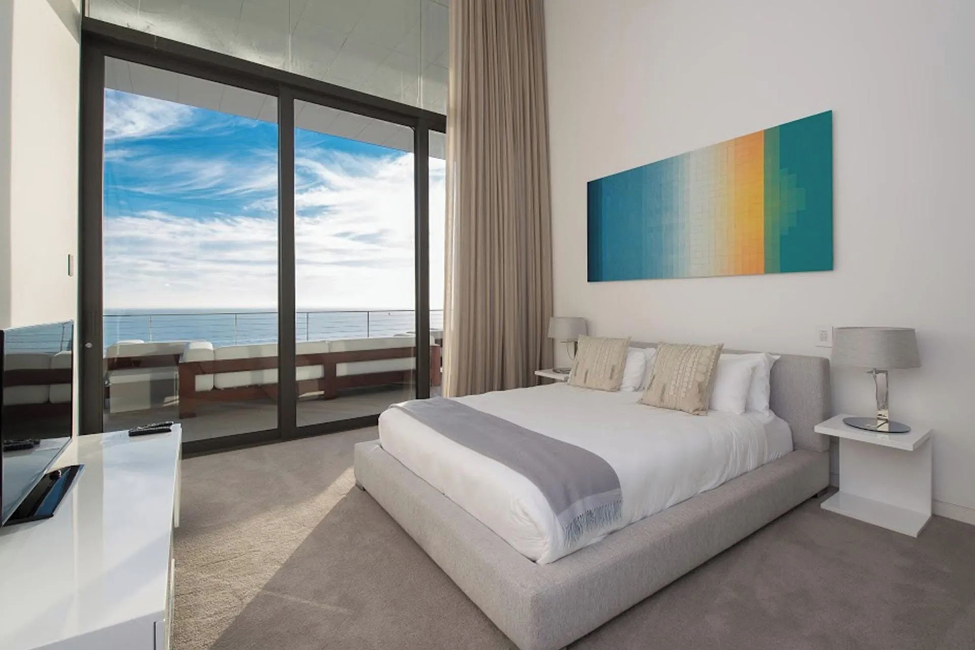 Et hotelværelse med en stor seng, et skrivebord, en stol, et natbord, en lampe, et billede og havudsigt.
