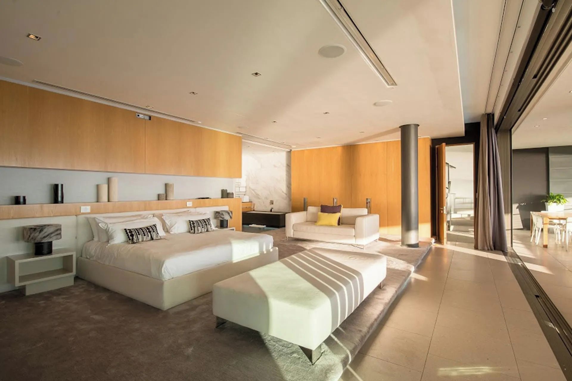 Ein modernes Hotelzimmer mit einem großen Bett, einem Sofa, einem Couchtisch und Blick ins Freie.