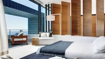 Un dormitorio moderno con una cama grande, una zona de estar con sofá y mesita auxiliar, y vista al océano.