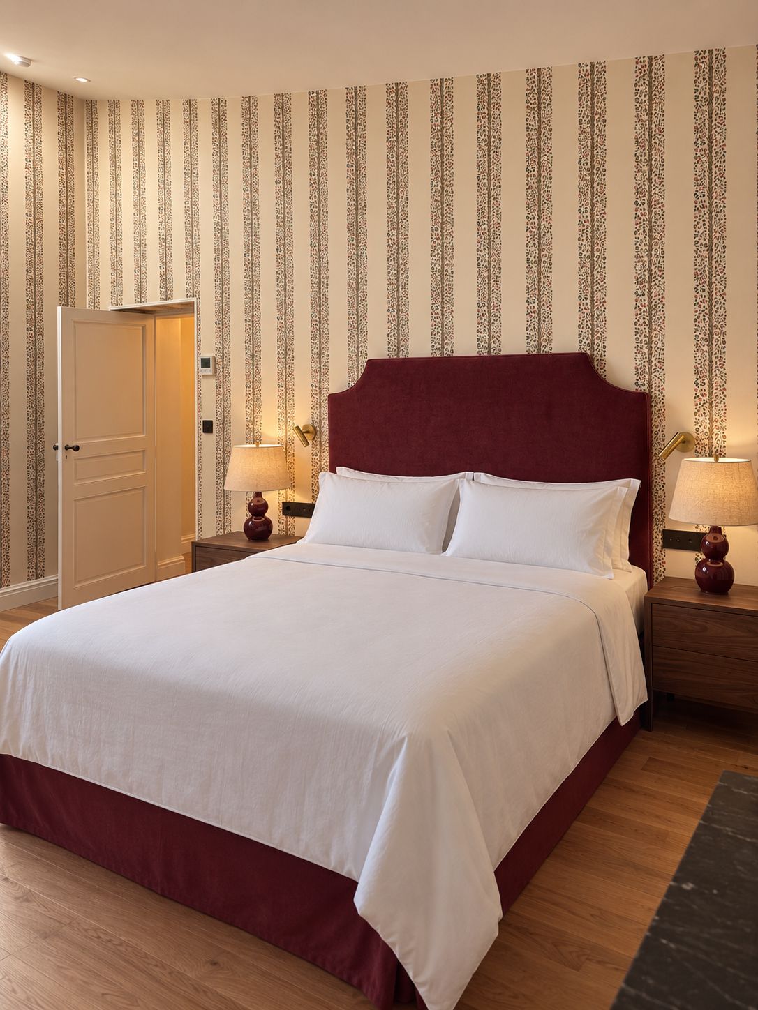 A hotel room with a large bed, two bedside tables with lamps, a door, and patterned wallpaper.