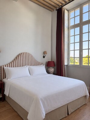 Una cama con ropa de cama blanca, un cabecero a rayas y una mesita de noche con una lámpara.