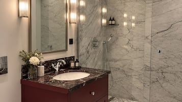 A modern bathroom with a marble sink, a large mirror, and a walk-in shower.