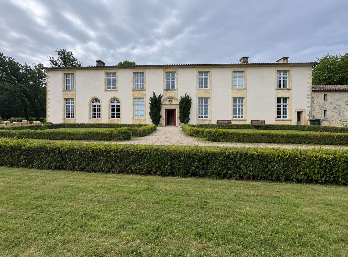 Un grand bâtiment symétrique, doté d’une entrée centrale, entouré de haies bien entretenues et d’une pelouse verdoyante.