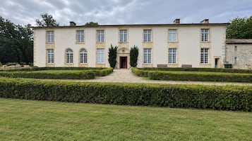 Un grand bâtiment symétrique, doté d’une entrée centrale, entouré de haies bien entretenues et d’une pelouse verdoyante.