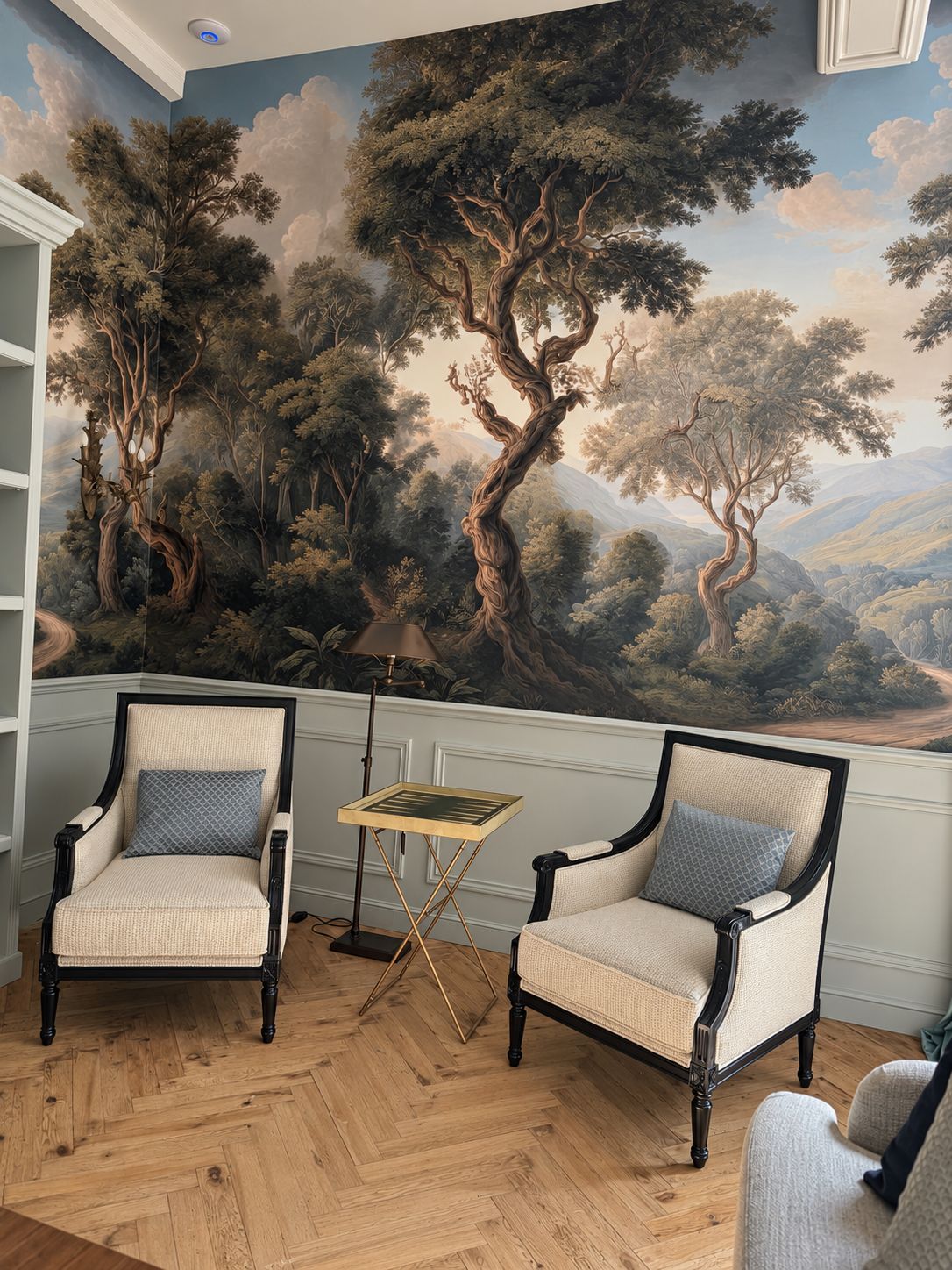 A room with two armchairs, a small table, and a mural of trees on the wall.
