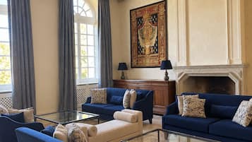 A spacious living room with a high ceiling, large windows, and a fireplace.