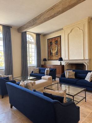 Een ruime woonkamer met een hoge plafond, grote ramen en een open haard.