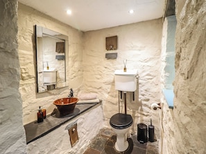 Ein Badezimmer mit Steinwand, Waschbecken aus Holz, Toilette und Spiegel.