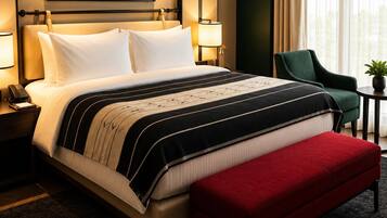 A hotel room with a large bed, bedside lamps, a red bench, a green chair, and a view of the outdoors through a window.