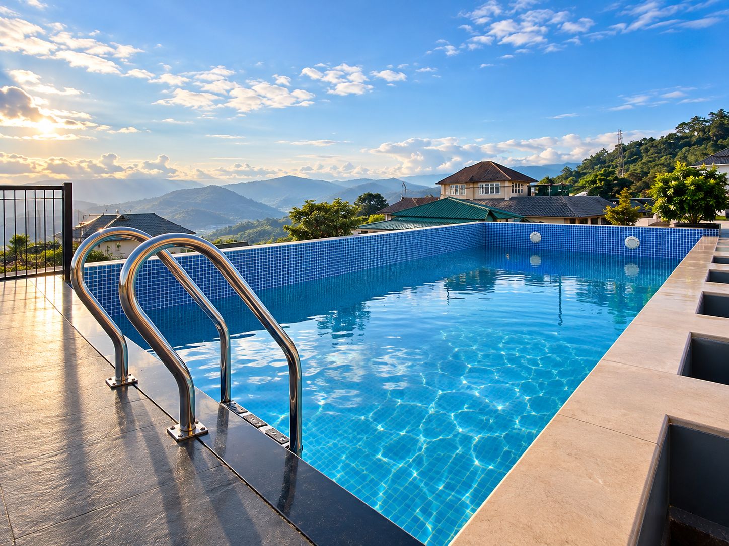Piscina azul cristalina con barandillas metálicas, rodeada de un suelo de baldosas y con vistas a un paisaje montañoso.