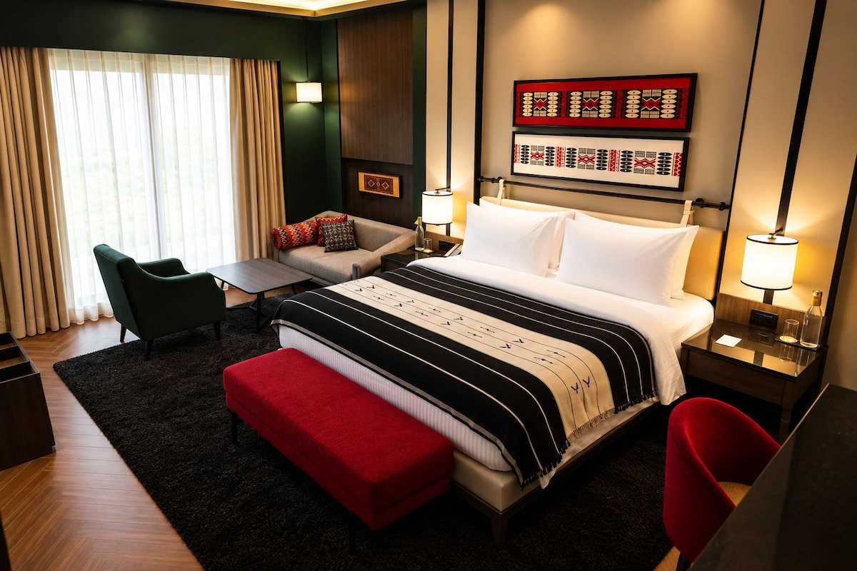 Quarto de hotel com cama, sofá, um banquinho vermelho, escrivaninha e cadeira.