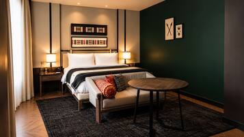 Una habitación de hotel con una cama, mesitas de noche, una mesa redonda y una pared de acento verde oscuro.