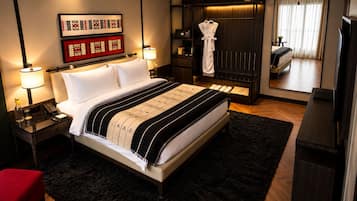 Habitación de hotel con una cama grande, lámparas de noche, una silla roja, un armario y un espejo que refleja la habitación.