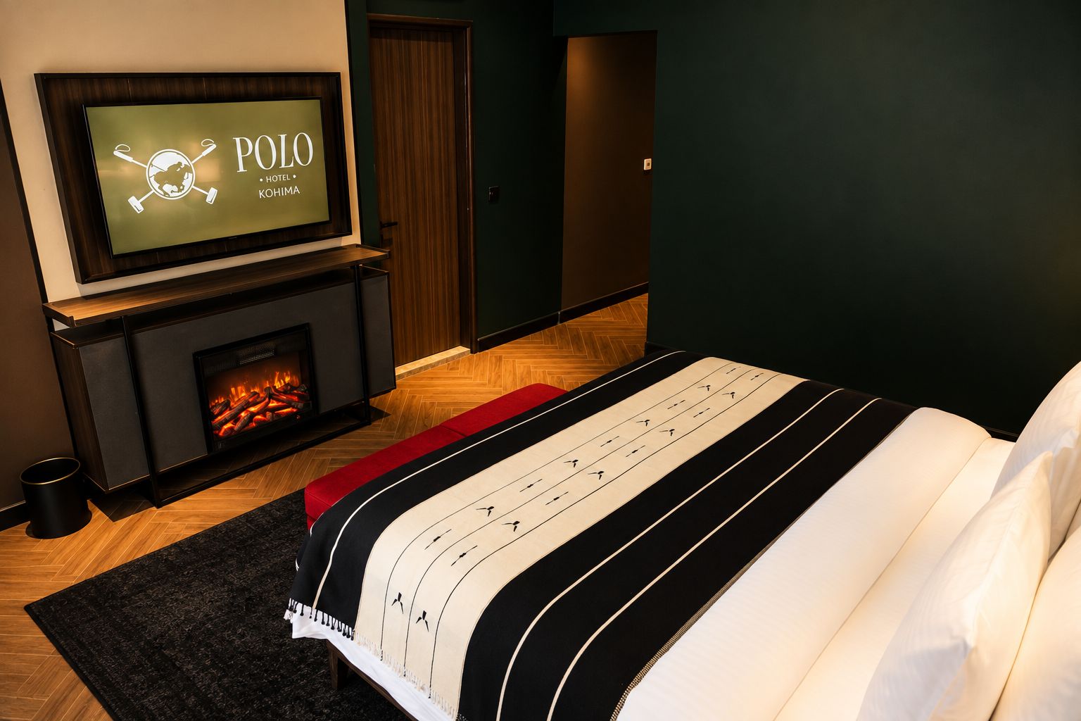 Ein Hotelzimmer mit Fernseher, der den Hotelnamen anzeigt, Kamin, Bett mit Streifenmusterdecke und Holzboden.