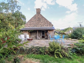 Une maison en pierre avec un toit à deux versants, un porche à l’avant doté de sièges et un foyer extérieur en pierre.