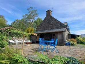 A rustic stone building with a chimney, outdoor seating area with blue chairs, and a stone patio. - Waen Fechan (Dolgellau)