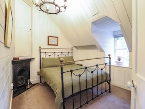 A bedroom with a sloped ceiling, a bed with a metal frame, a fireplace, and a window with a view. - Waen Fechan (Dolgellau)