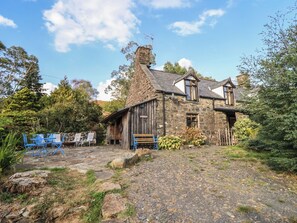 A stone house with a gravel driveway, a wooden bench, and blue chairs. - Waen Fechan (Dolgellau)