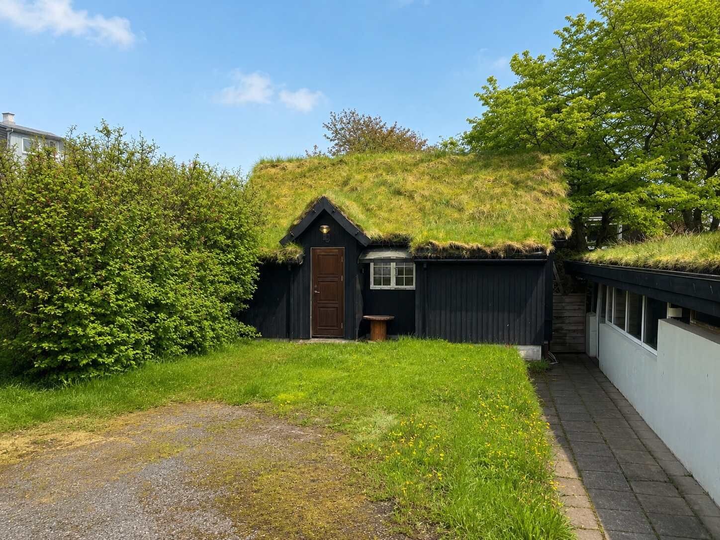 A thatched-roof building with a door and windows, surrounded by greenery and a paved path.