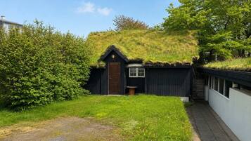 A thatched-roof building with a door and windows, surrounded by greenery and a paved path.
