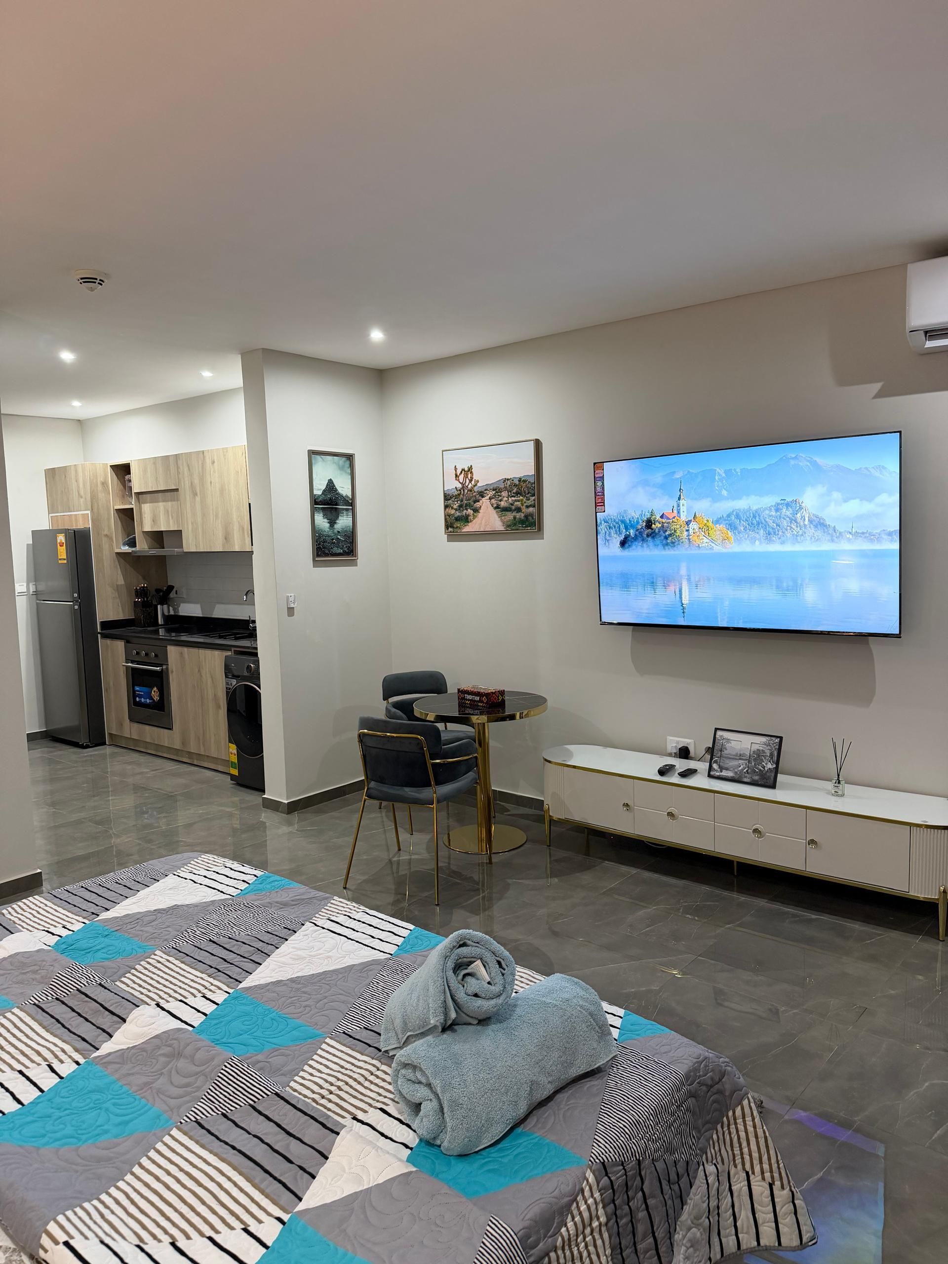 A modern living room with a flat-screen TV, a sofa, a dining table, and a kitchen area.