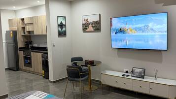 A modern living room with a flat-screen TV, a sofa, a dining table, and a kitchen area.