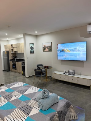Una sala de estar moderna con televisor de pantalla plana, un sofá, una mesa de comedor y una zona de cocina.
