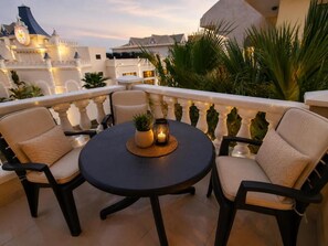 Ein Balkon mit rundem Tisch und vier Stühlen, umgeben von einem weißen Geländer.