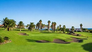 Ein Golfplatz mit blauem Himmel, Palmen und Blick aufs Meer.