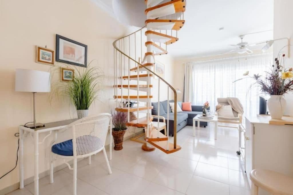 Una sala de estar moderna con una escalera en espiral, un conjunto de sofá, un comedor y una planta en maceta.