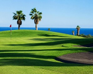 A golf course with a flag, palm trees, and a view of the ocean. - Golf Park Sunny Cozy Penthouse Near the Ocean (San Miguel de Abona)