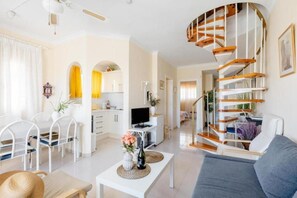 Ein modernes Wohnzimmer mit einer geschwungenen Treppe, weißen Möbeln und einem Essbereich mit Stühlen und einem Tisch.