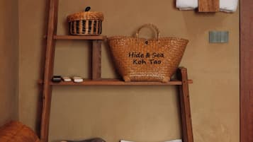 A wooden ladder shelf with a woven basket, a tote bag, and folded towels against a beige wall.