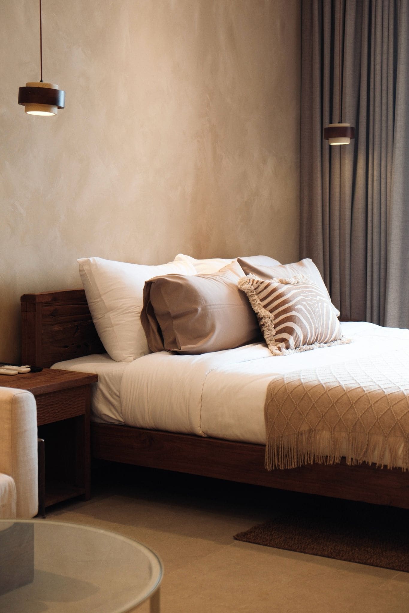 A modern bedroom with a bed, nightstands, a round table, and a hanging light fixture.