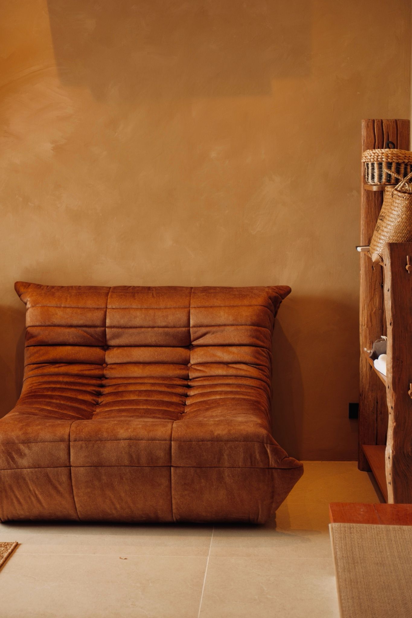 A bed with a tufted headboard in a room with a wooden wall and a woven basket on a shelf.