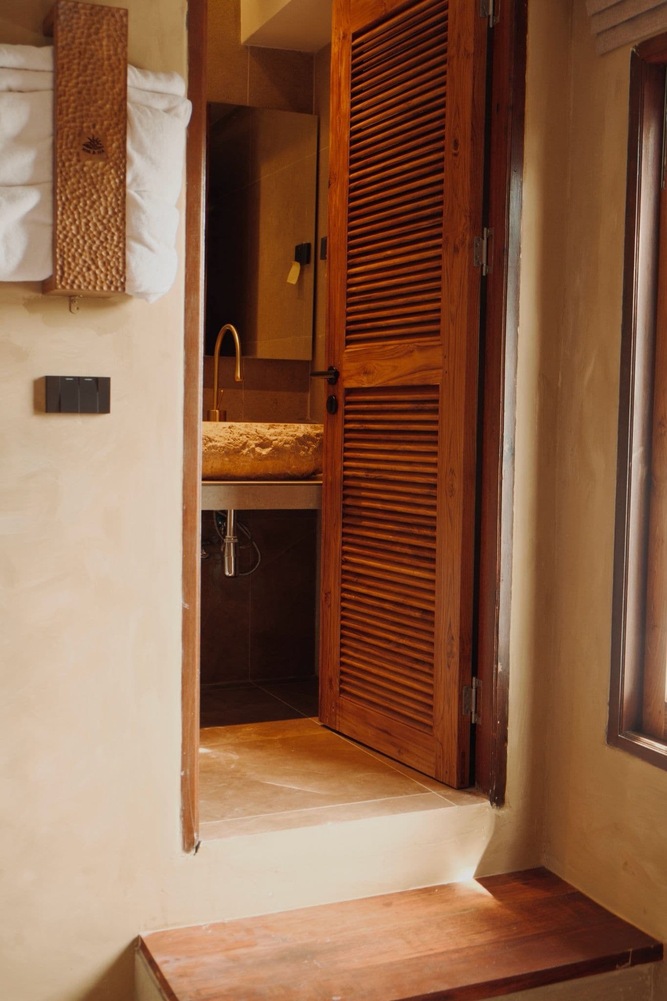 A wooden door leading to a bathroom with a sink and towel rack.