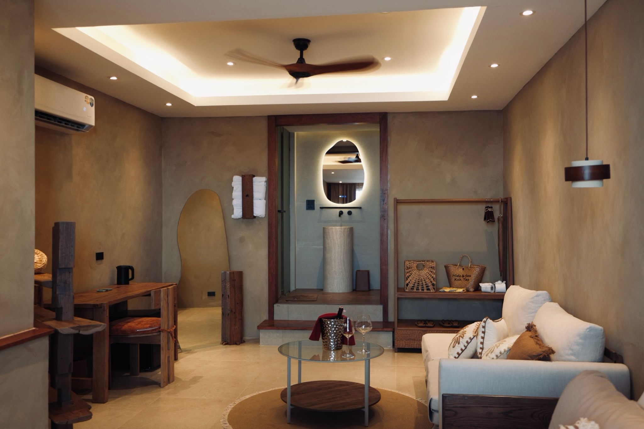A modern living room with a glass coffee table, a sofa, a wooden side table, and a ceiling fan.