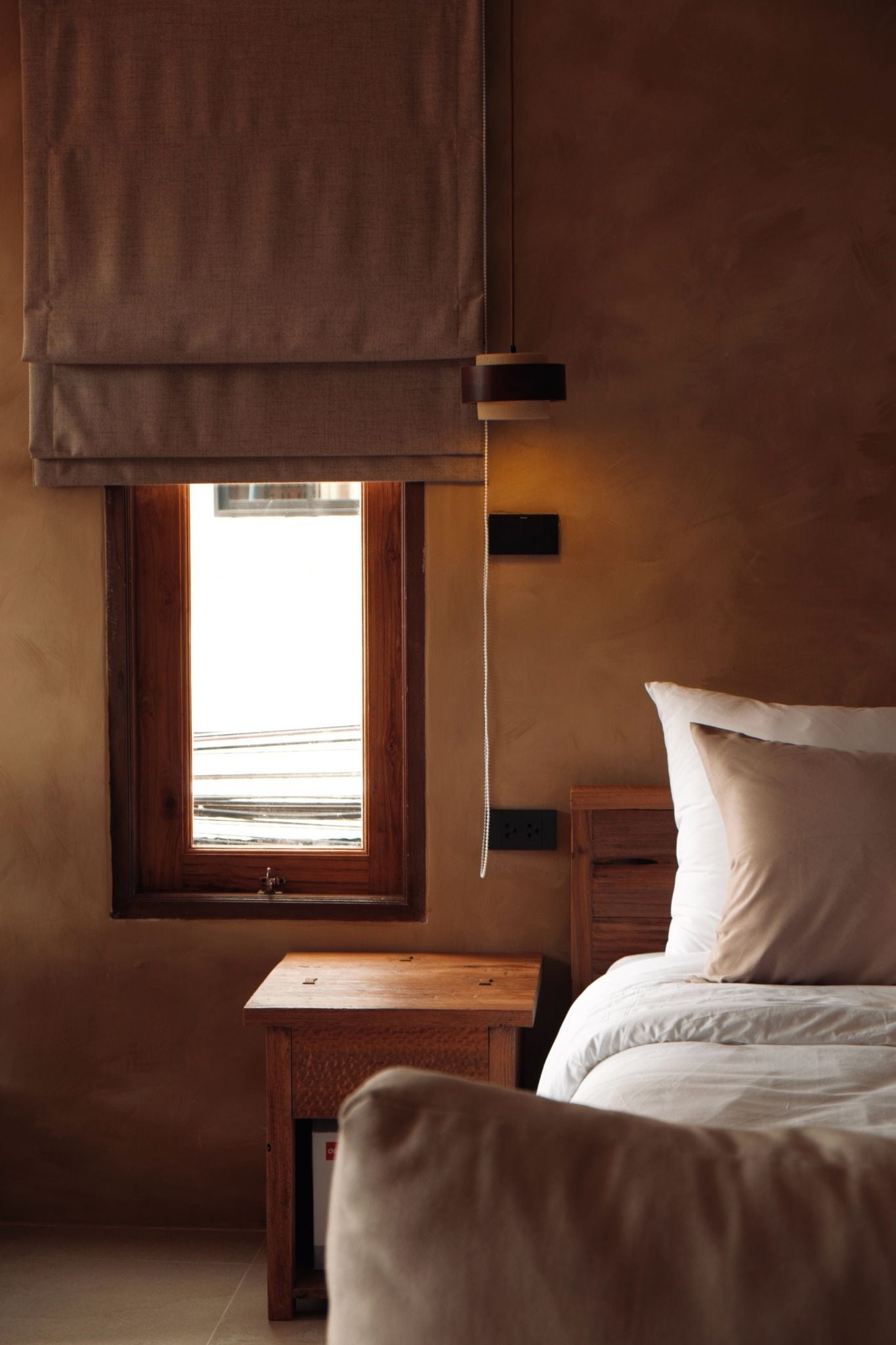 A bedroom with a window, a bedside table, a bed, and a hanging light fixture.