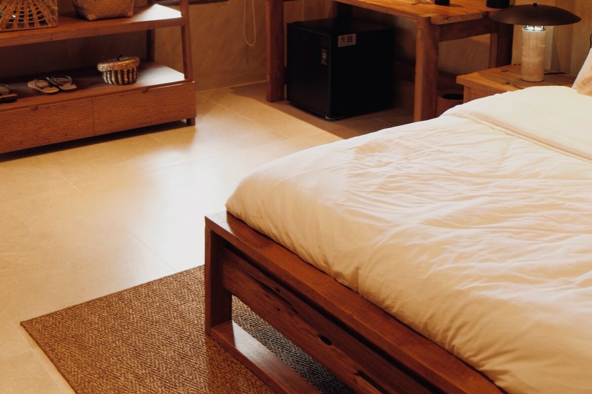 Un dormitorio con una cama, un escritorio, una silla, una lámpara y un refrigerador pequeño.