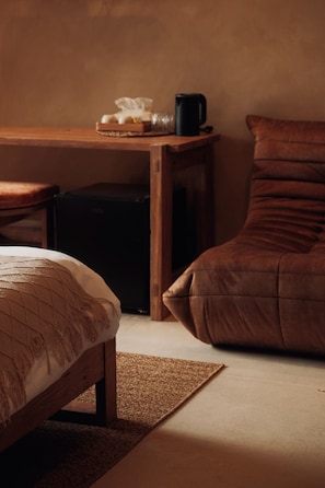 Una habitación acogedora con una cama, una mesita con una caja de pañuelos y una taza negra, una silla y una alfombra.